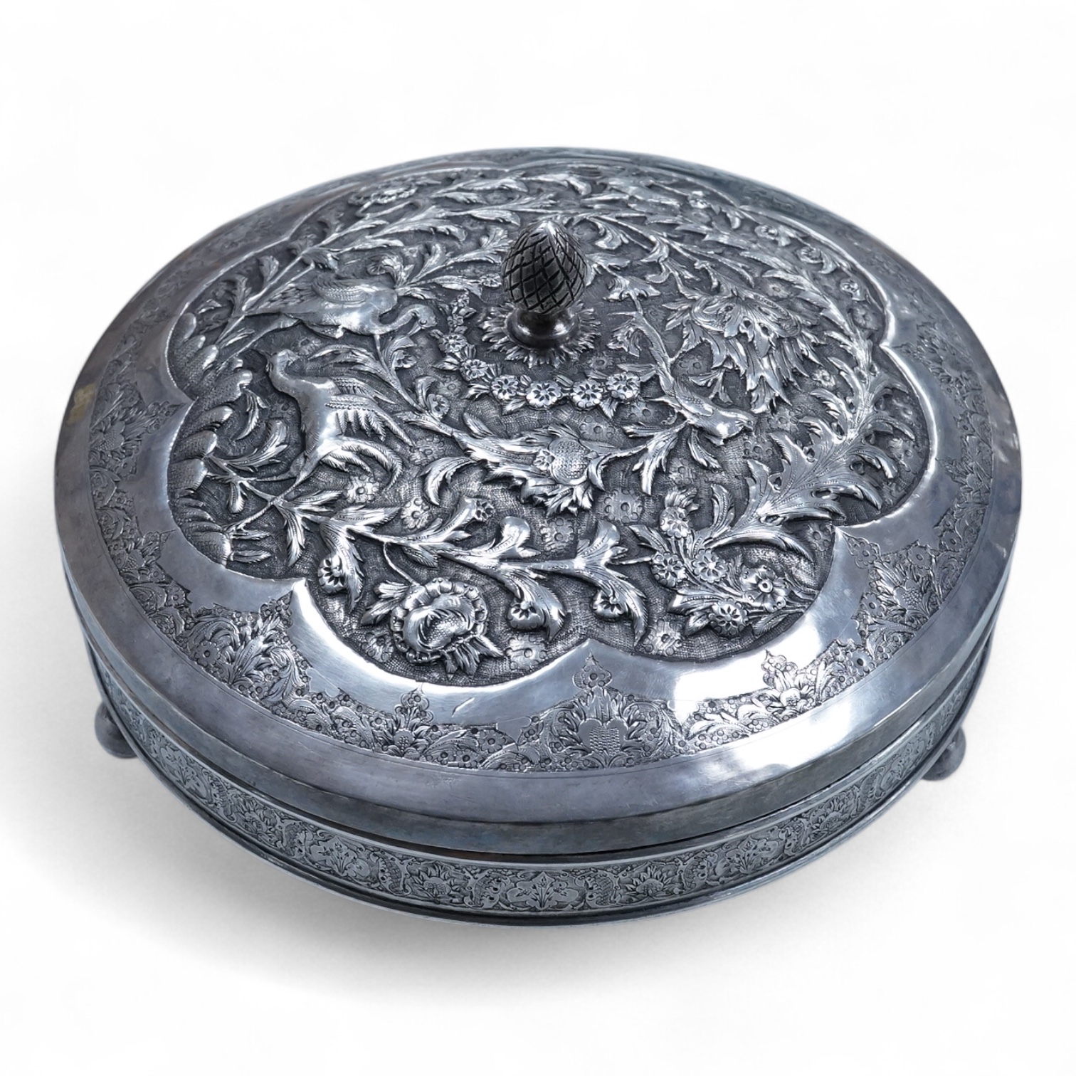 A 20th century Middle Eastern white metal circular box and cover, decorated with birds amongst foliage, base diameter 21.8cm, on three bun feet, 31.7oz.
